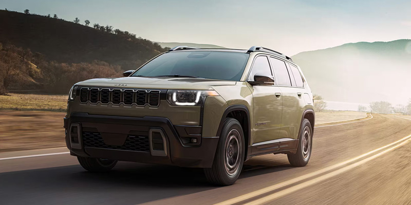 A green Jeep Cherokee driving on a road through a mountainous landscape with clear skies.