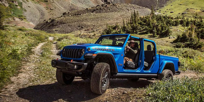 2026 Jeep Gladiator driving off-road on a dirt trail in the mountains.