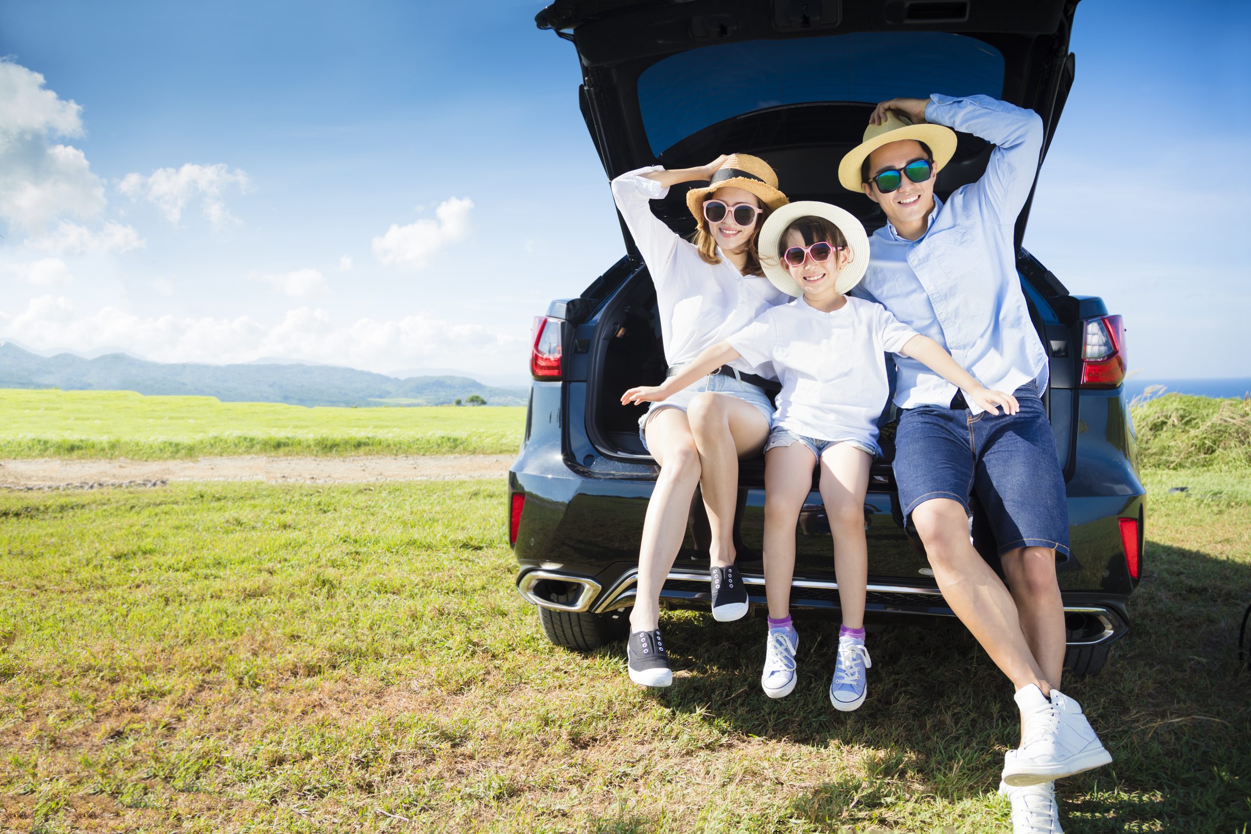 Family sitting in SUV trunk enjoying outdoor picnic.