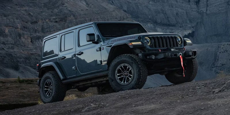 Black Jeep Wrangler Rubicon climbing rugged terrain with rocky mountains in the background.